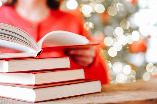 Christmas reading.Christmas books. Woman Turning Pages of a Book by Christmas Tree Lights for holiday reading lists,book clubs,winter leisure and educational content. 