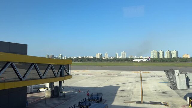 View of an aircraft on the runway and apron from inside Vitória Airport terminal, with the city skyline in the background