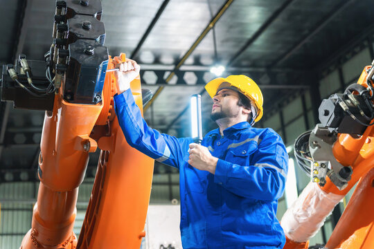 Robotics engineer repairing and maintaining industrial robot arm, technician servicing robotic machine in automated manufacturing factory plant, automation worker checking mechanical equipment