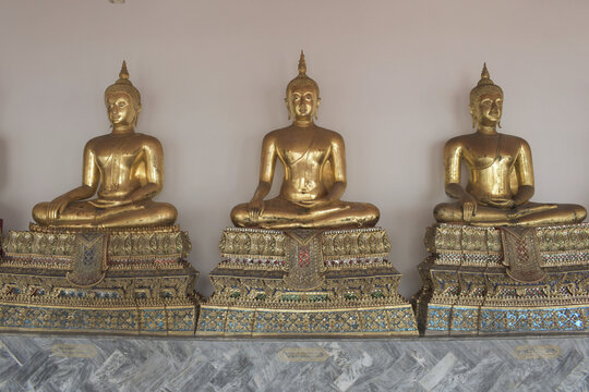 three golden buddha statues seated on richly decorated traditional pedestals