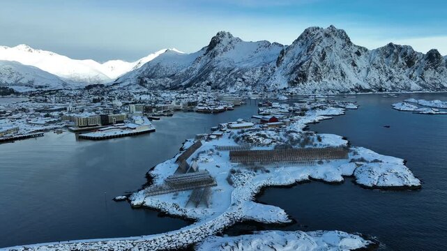 Aerial view of Svolvaer harbor with snow-covered mountains, traditional fish drying racks, and coastal buildings in Svolvaer, Nordland, Norway.