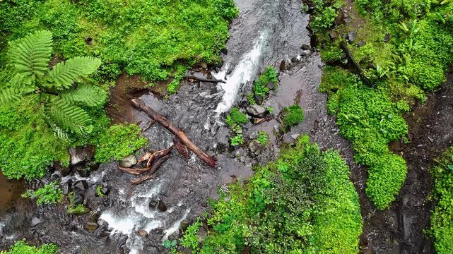 Aerial view of Curug Ciarjuna waterfall flowing through lush tropical forest with rocky riverbed and dense green vegetation in Garut, West Java, Indonesia.
