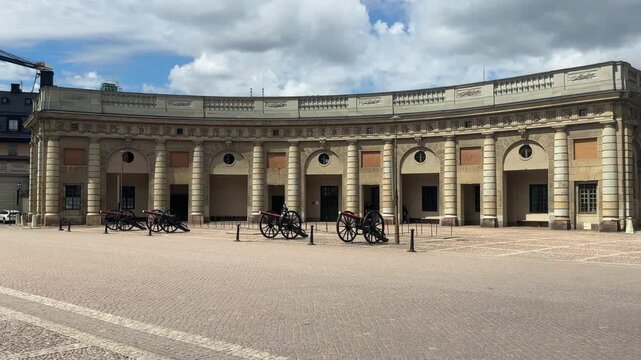 Wide locked-off shot of the curved classical colonnade and historic artillery cannons in the outer courtyard of the Stockholm Royal Palace on Gamla Stan.