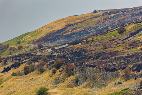 Burnt moorland vegetation covering steep hillside above limestone crags, smoke drifting over damaged landscape following severe wildfire outbreak