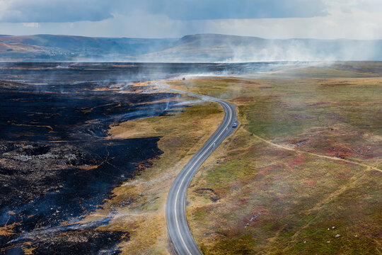 High angle shot of a road dividing burnt heathland from unburned pasture, wildfire destruction threatening natural habitats