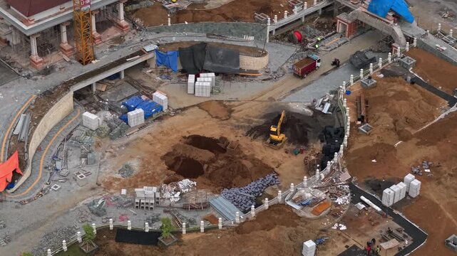 Aerial view of building construction site with heavy machinery, piles of materials, and earthworks in Gianyar, Bali, Indonesia.