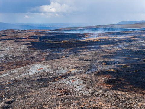 High angle view over charred moorland terrain, residual smoke drifting past burnt vegetation, environmental impact of grass fires in upland ecosystems