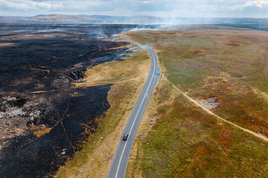 Wide drone perspective of mountain pass split by wildfire damage, burned earth bordering grassy hills, highlighting wild land vulnerability