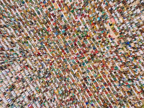 Aerial view of a large crowd of people gathered for Eid prayer on colorful prayer mats in an open field in Narayanganj, Dhaka, Bangladesh.