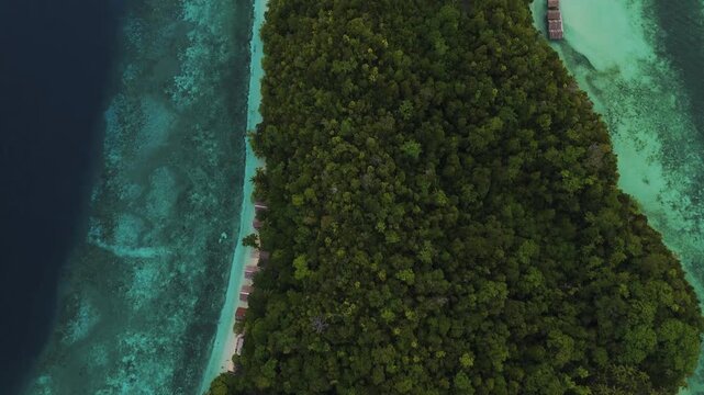 Aerial view of Mios Kri island with lush tropical forest, turquoise waters, and overwater bungalows in West Supiori, Papua, Indonesia.