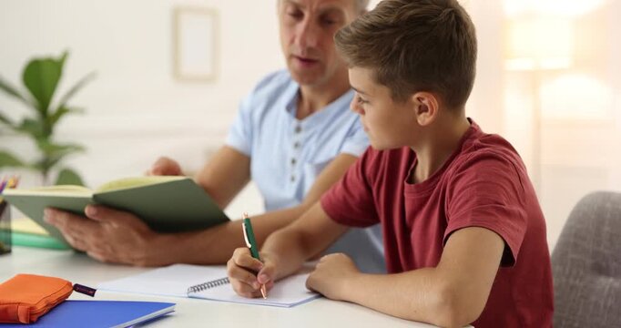 Father with book helping his son with homework at white table indoors, selective focus