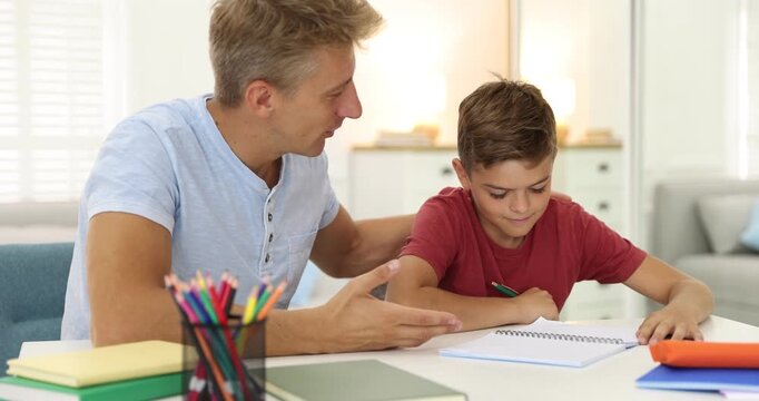 Father helping his son with homework at white table indoors