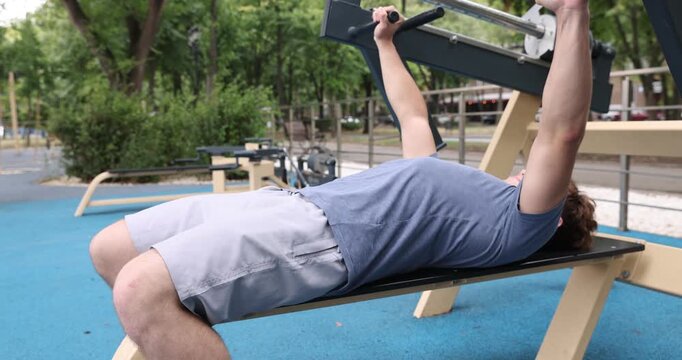 Teenage boy exercising on bench press machine at outdoor gym
