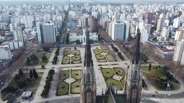 Dynamic drone path gliding quickly between the main spires of La Plata Cathedral, revealing Plaza Moreno and the Municipal Palace. Argentina.