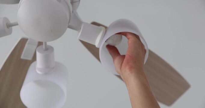 Man replacing light bulb in ceiling fan at home, closeup. Low angle view