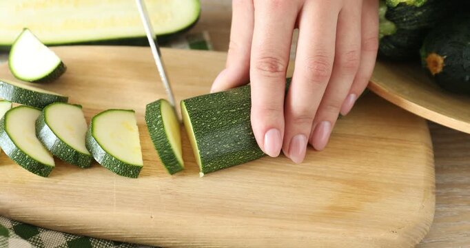 Woman cutting fresh zucchini with knife at wooden table, closeup
