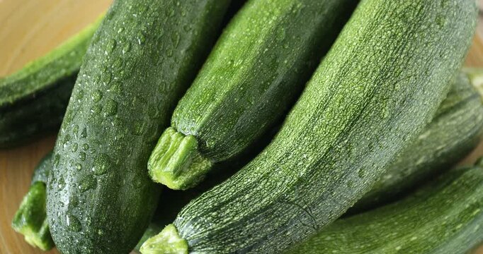 Many fresh raw zucchinis with water drops spinning on plate, closeup
