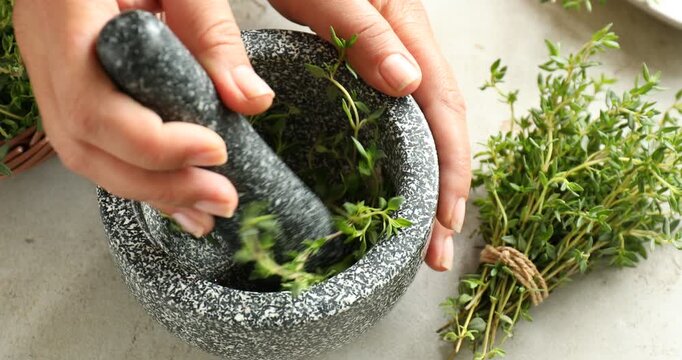 Woman putting fresh thyme into mortar and crushing it with pestle at light table, closeup