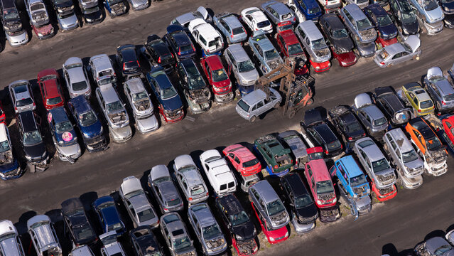 Aerial view of a car scrapyard in Gdansk, Poland, featuring rows of wrecked vehicles and a forklift moving a car.