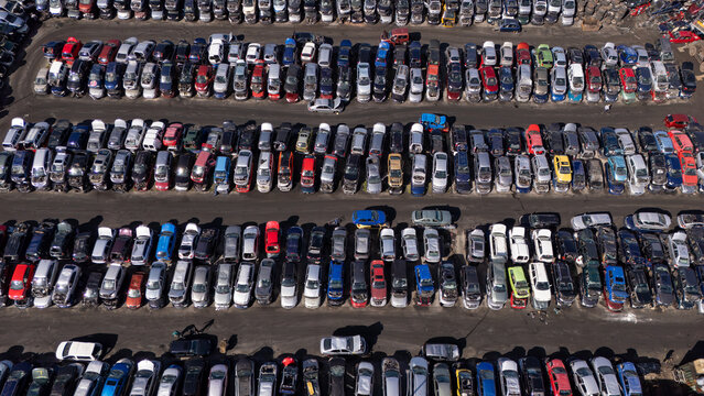 Aerial view of a large car salvage yard with rows of parked vehicles in various colors arranged on an asphalt lot in Gdansk, Poland.