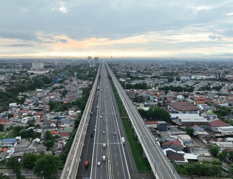 Aerial view of the Jakarta-Cikampek Toll Road and elevated railway track passing through dense urban residential areas in Bekasi Barat, West Java, Indonesia.