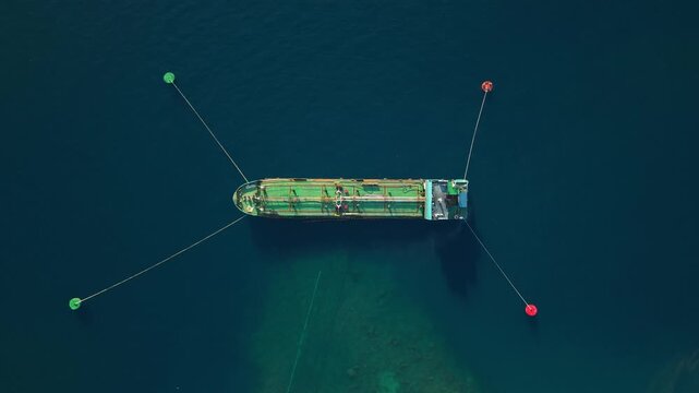Aerial view of a cargo ship moored in deep blue water and secured by four buoys in Buleleng, Bali, Indonesia.