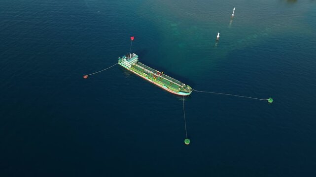 Aerial view of a tanker ship moored in the open sea with floating buoys and calm blue water in Buleleng, Bali, Indonesia.