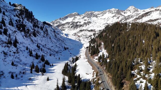 Aerial view of the winding road through the snow-covered Arlberg mountain pass with dense pine forests and steep slopes in Bludenz District, Vorarlberg, Austria.