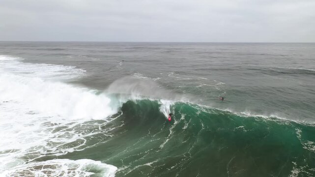 Aerial view of surfer catching large ocean wave on cloudy day.