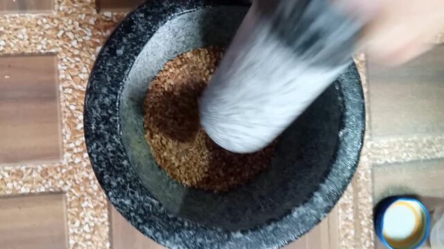 Grinding roasted rice powder with a traditional stone mortar and pestle for Thai cooking