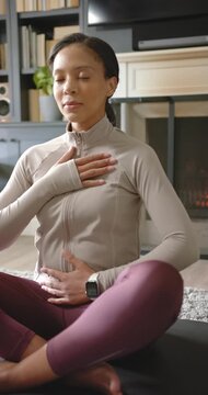 Vertical video: African woman in top closing eyes hands on chest breathing for calm on mat at home