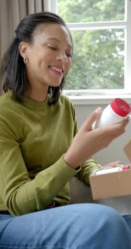 Vertical video: Adult woman on sofa opening box lifting bottle red cap checking label