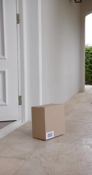 Vertical video: Door opening, woman with phone reaching barcode box on porch, retrieving delivery