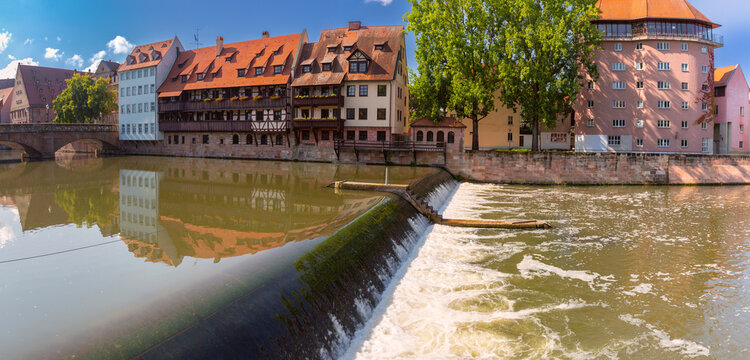 Traditional riverside buildings reflected in the Pegnitz River beside a weir on a sunny summer day in Nuremberg, Germany.