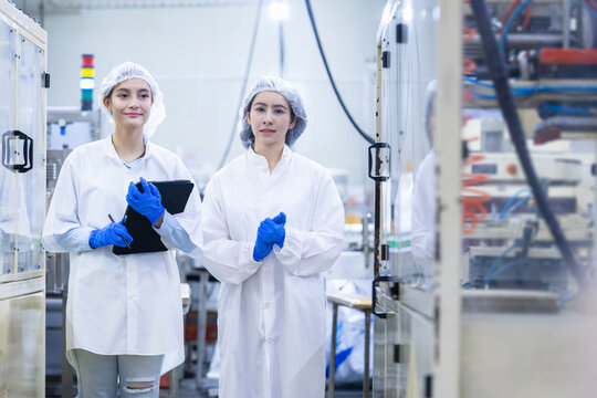 Female quality control inspectors working together in food factory plant, factory workers in protective uniform and hairnet checking manufacturing plant