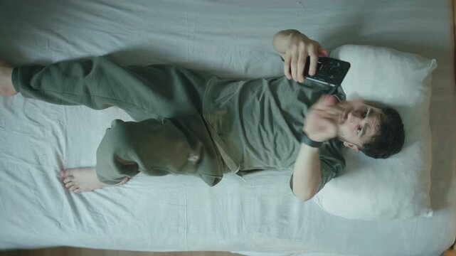 Man overwhelmed by phone scrolling in bed, tired eyes and social media fatigue