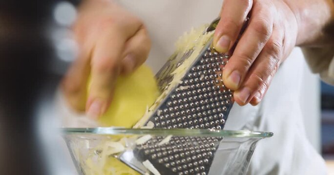 Grating fresh potato into a glass bowl for cooking preparation.