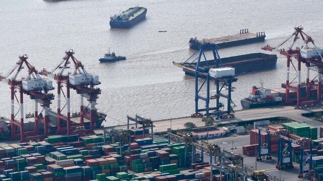Industrial cargo ships moving through the river near the busy container terminal at daytime