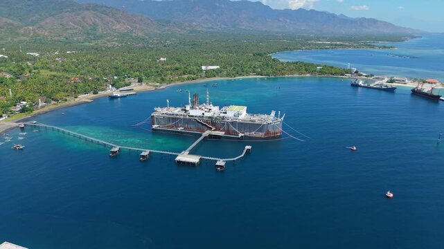 Aerial view of the Cinta Natomas Floating Storage and Offloading ship anchored in the clear blue waters with a pier extending to the coastline of Buleleng Regency, Bali, Indonesia.