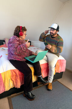 An adult man asks his mother if she can hear the music through his red headphones