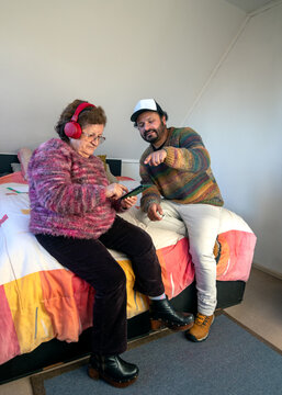 An elderly woman wearing red headphones is learning how to listen to music on a cell phone with her son's help