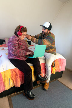 An active senior woman listens to music through headphones on a laptop with her son's help