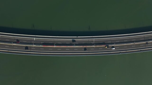 Aerial view of the Bali Mandara Toll Road crossing the water with cars driving on the asphalt surface in Kecamatan Kuta Selatan, Bali, Indonesia.