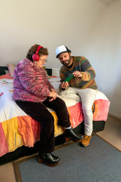 An adult man teaches his elderly mother how to listen to music using headphones and a cell phone