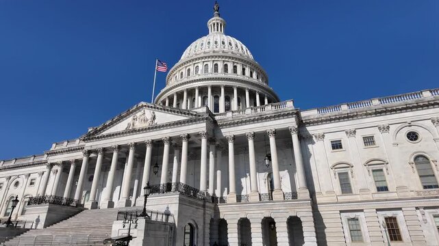 Low angle dolly shot moving past the U.S. Capitol building and iconic dome under a deep blue sky in Washington, DC. 15348  
