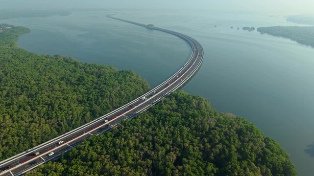 Aerial view of Bali Mandara Toll Road crossing over the water through lush mangrove forests with cars driving on the highway in Kecamatan Kuta Selatan, Bali, Indonesia.