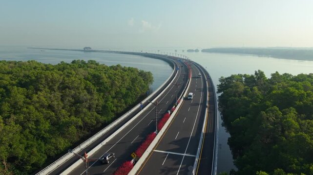 Aerial view of the Bali Mandara Toll Road stretching over the water, surrounded by lush mangrove forests in Kecamatan Kuta Selatan, Bali, Indonesia.