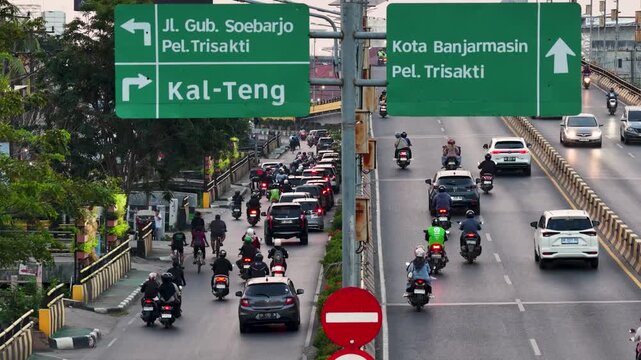 Vehicles and motorcycles travel on a multi lane road with clear directional signs in the city