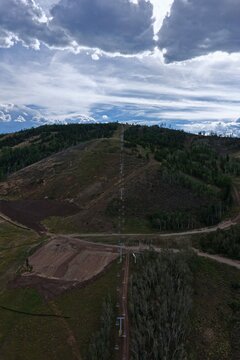 Aerial view of the chairlift line ascending the mountain slope at Granby Ranch, featuring forested areas, dirt trails, and a cloudy sky in Granby, Colorado, United States.