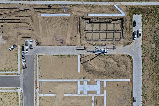 Aerial view of a residential construction site featuring concrete foundation work, a concrete pump truck, and various construction vehicles on a dirt lot in Westminster, Colorado, United States.